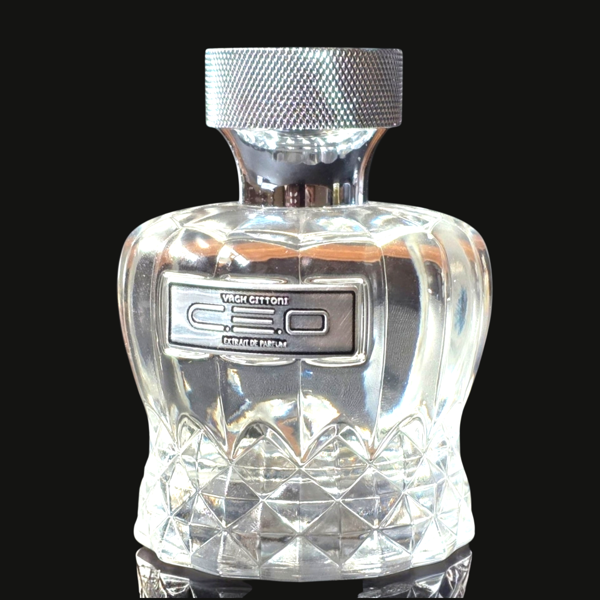 Clear perfume bottle with diamond cut design and silver cap on a black background